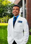 Student posing on campus in white coat