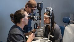 Optometry students perform an eye exam using diagnostic equipment during hands-on clinical training.