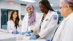 Pharmacy students in lab coats work together at a lab bench preparing and analyzing materials during hands-on training.
