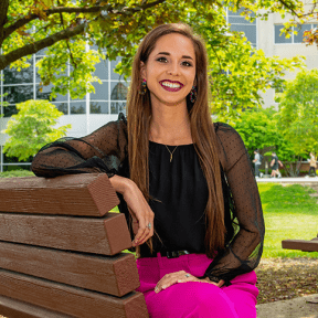 woman sitting on a bench outside, smiling for a picture