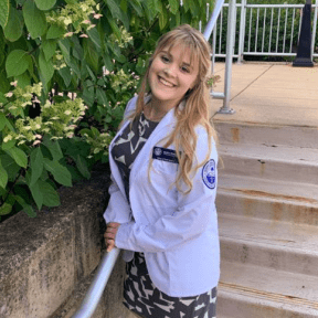 Student posing on stairs in white coat