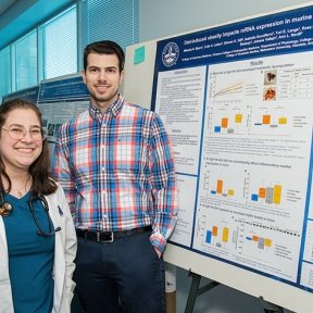 Two students displaying large research poster and findings