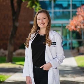 Taylor Alflen posing outside on campus in white coat.