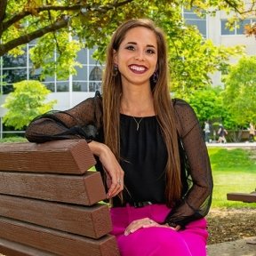 Woman sitting on a bench outside, smiling for a picture