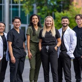 Six Midwestern University students wearing white coats and scrubs.