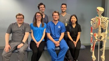 Six AZCOM Scholars sitting on bench near skeleton.