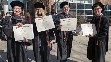 Four College of Pharmacy graduates holding their diplomas.