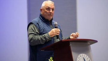 Rudy Ruettiger delivers a speech at a podium during an evening event.