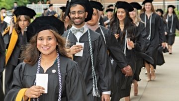 Graduates line up for the processional in black caps and gowns carrying their name cards in their hands.