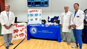 Dr. Durso, Dr. Williams, and dental student William Boensch in white coats in front of their booth at the Senior Fair in Lemont.