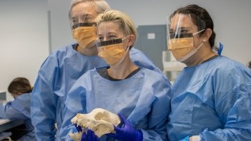 Three people in medical protective gear. One holding animal skull