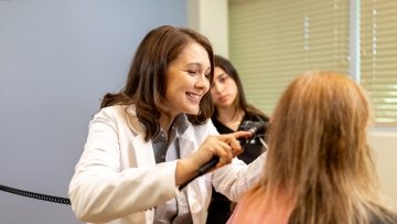 Medical professional examining a patient’s ear with an otoscope while another person observes in a clinical room.