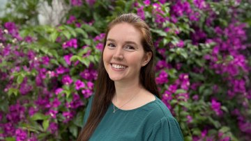Jenna Hoover smiles at the camera in front of purple-flowered bushes