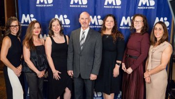 Faculty from the Arizona College of Osteopathic Medicine stand in front of a banner at a March of Dimes event