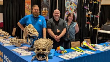 Three anatomy professors stand behind Midwestern's Fan Fusion booth, with various real and fictional skulls on the table