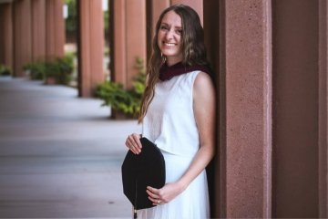 AnnaLisa West (SLP '26) stands with her graduation cap and masters hood on campus