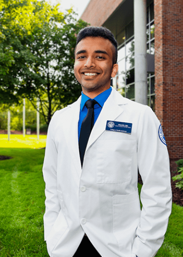 Student posing on campus in white coat