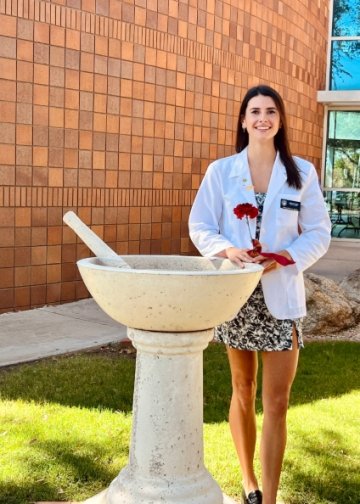 Gabriela Rajic stands in her white coat next to the pestle and mortar pharmacy statue