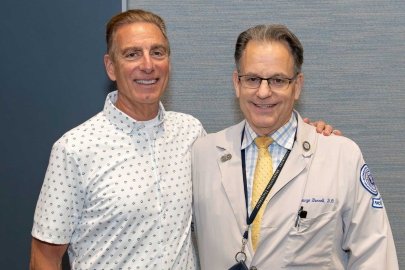 Mr. Giglio and Dr. Borelli in a white coat and stethoscope take a photo together at the patient panel.