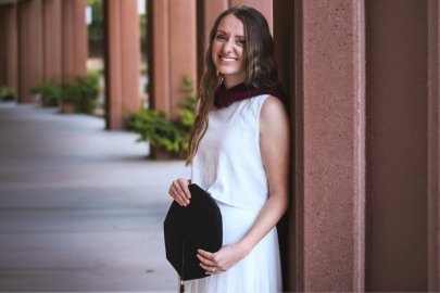 AnnaLisa West (SLP '26) stands with her graduation cap and masters hood on campus