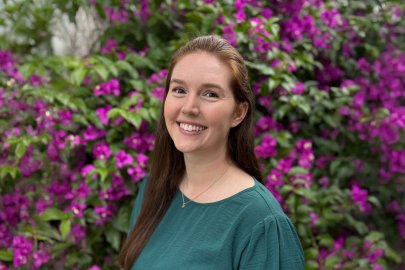 Jenna Hoover smiles at the camera in front of purple-flowered bushes