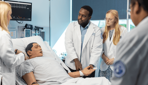 Students gathered around fake patient in simulation center while professor instructs