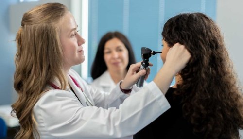 Student examining patient’s ear, while professor observes