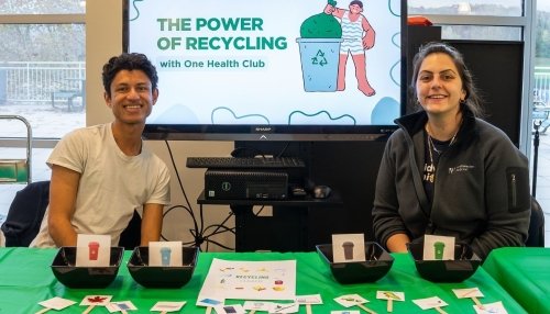 One Health Club members sit at a table with a “Power of Recycling” slide presentation on a monitor behind them.