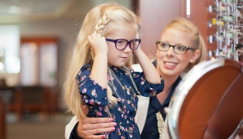 Girl trying on glasses in a mirror with help from a doctor