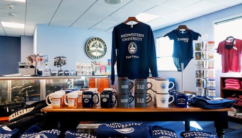 Display table of Midwestern University apparel and branded mugs inside the campus store, with folded clothing and merchandise arranged neatly.