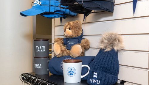 Shelf display featuring university mugs, knit hats with pom-poms, and a teddy bear dressed in Midwestern University-branded accessories.