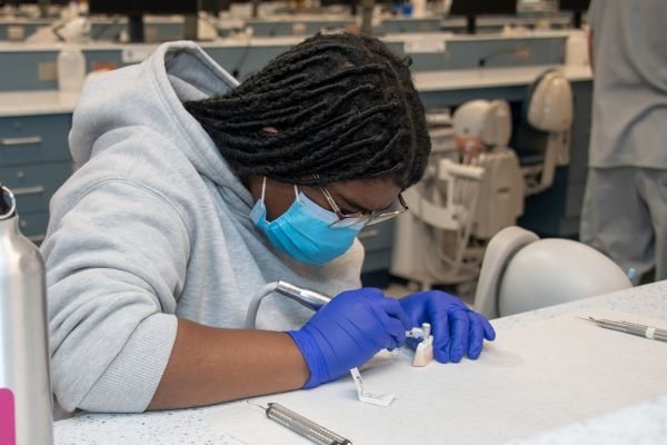 A high school student drills the mold of teeth in the dentistry session.