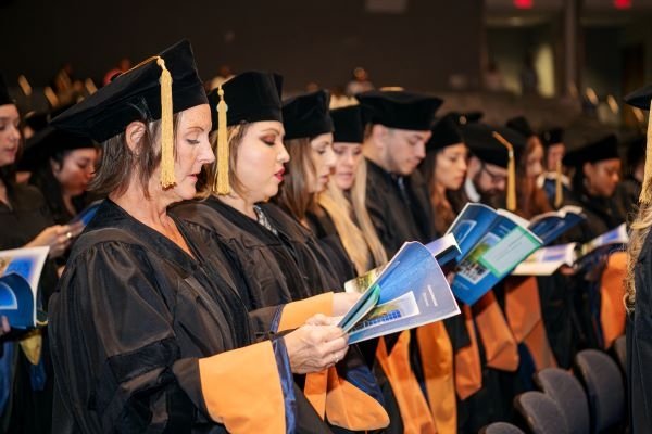 Graduates in black caps and gowns hold the blue Midwestern University graduation program and recite their healthcare oath.