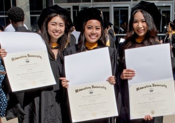 Three graduates stand together and display their diplomas from Midwestern University.