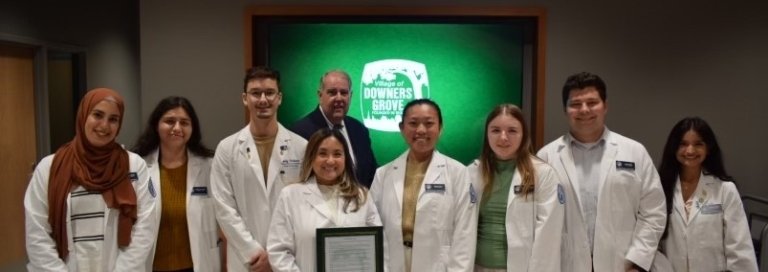 Pharmacy students, faculty pose for photo with white coats and proclamation.