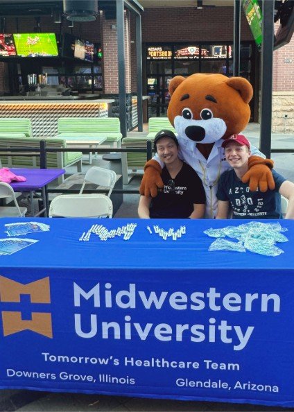 Two Midwestern students sit at a booth at the March of Dimes community walk with the mascot