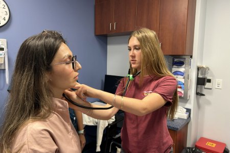 A high school student practices vital signs on a Midwestern student in a SIM Center exam room
