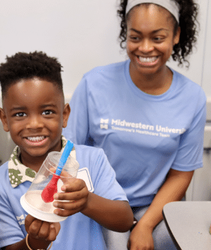 A kid shows off the lung model he made while his mother smiles in the background